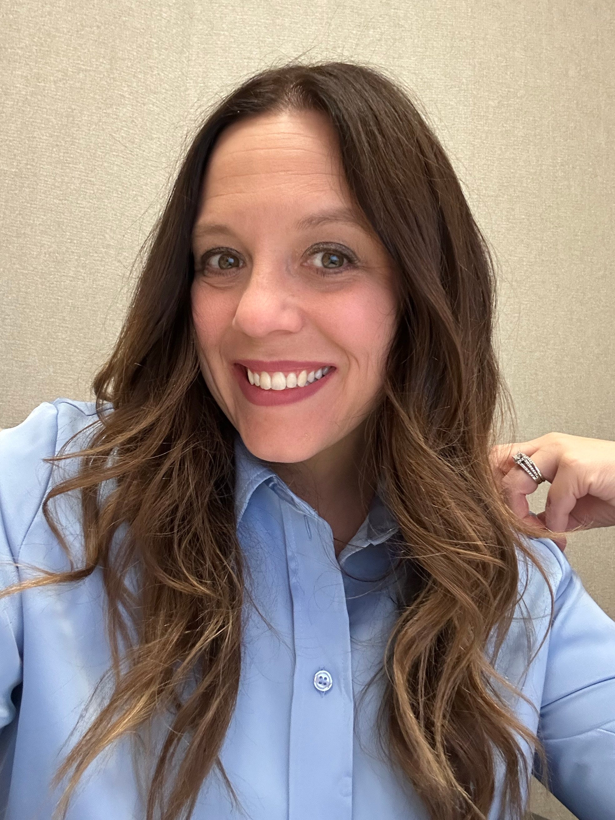 Woman with long brown hair wearing a light blue shirt against a beige wall.