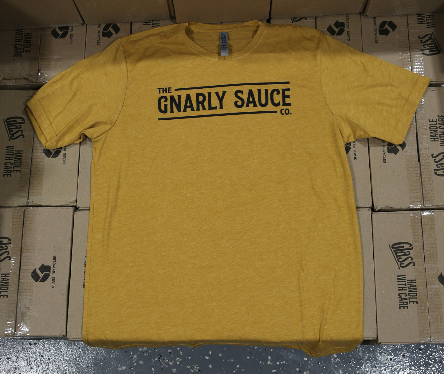 Yellow shirt with 'Gnarly Sauce company logo text in black on a stack of boxes