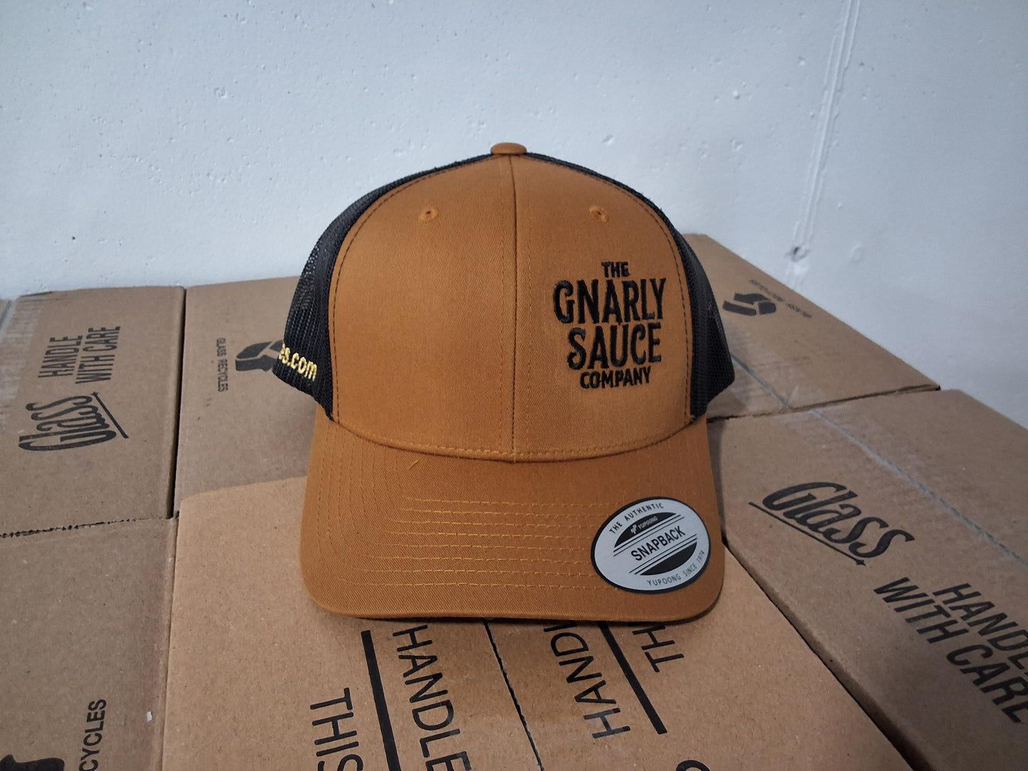 Brown and black cap with 'The Gnarly Sauce Company' logo in black on cardboard boxes.
