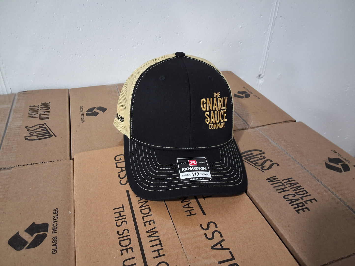 Black and yellow cap with 'The Gnarly Sauce Company' logo on cardboard boxes.